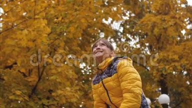 快乐的女孩在秋天在公园里扔黄叶，微笑着。 枫叶慢慢地落在地上的背景上